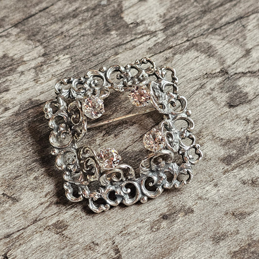 Ornate silver brooch with intricate filigree design and small gemstones.