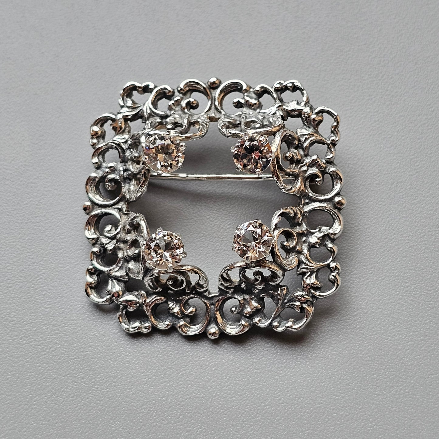 Ornate silver brooch with intricate scrollwork and small gemstones.