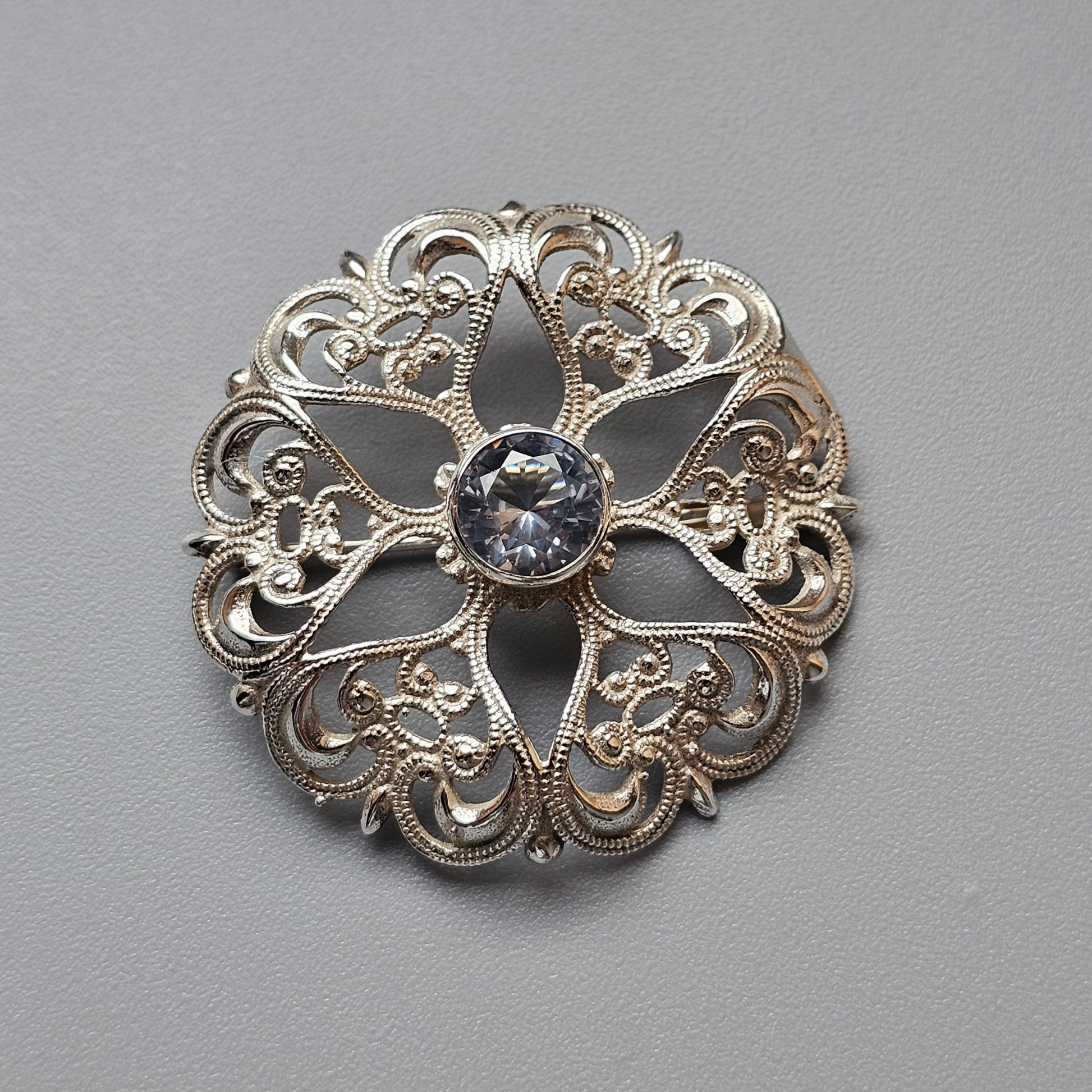 Ornate silver brooch with filigree design and central gemstone.