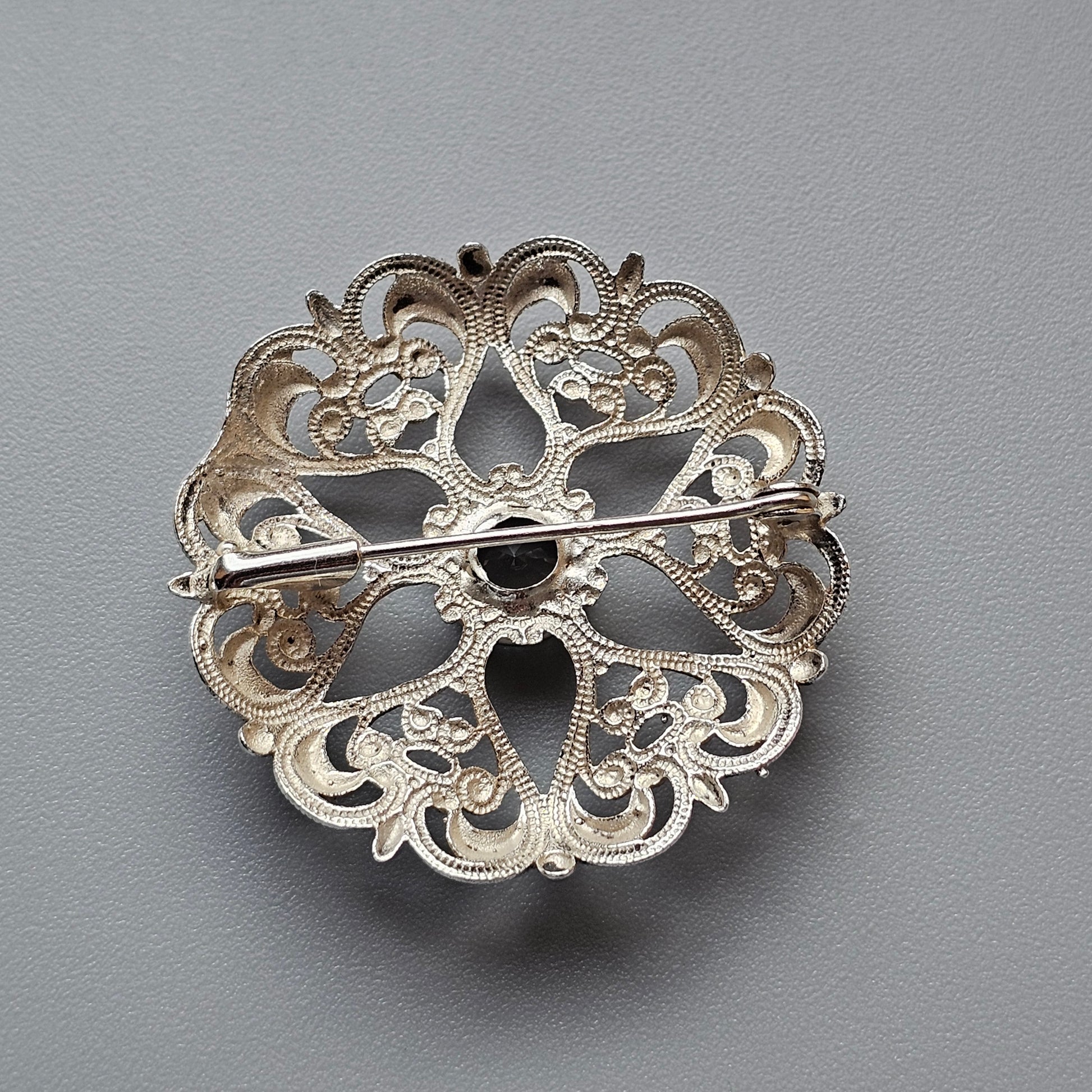 Ornate silver brooch with intricate filigree design in a circular shape.