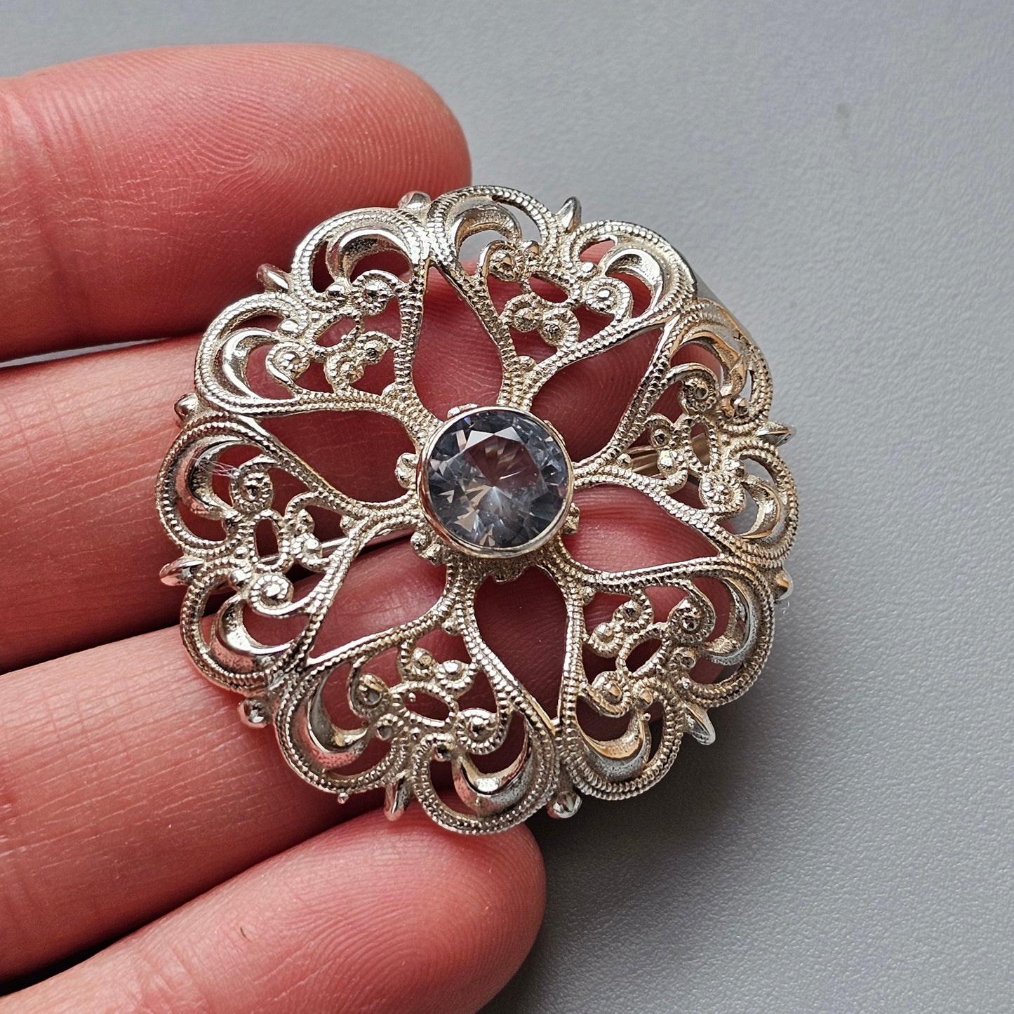 Ornate silver filigree brooch with a central gemstone.