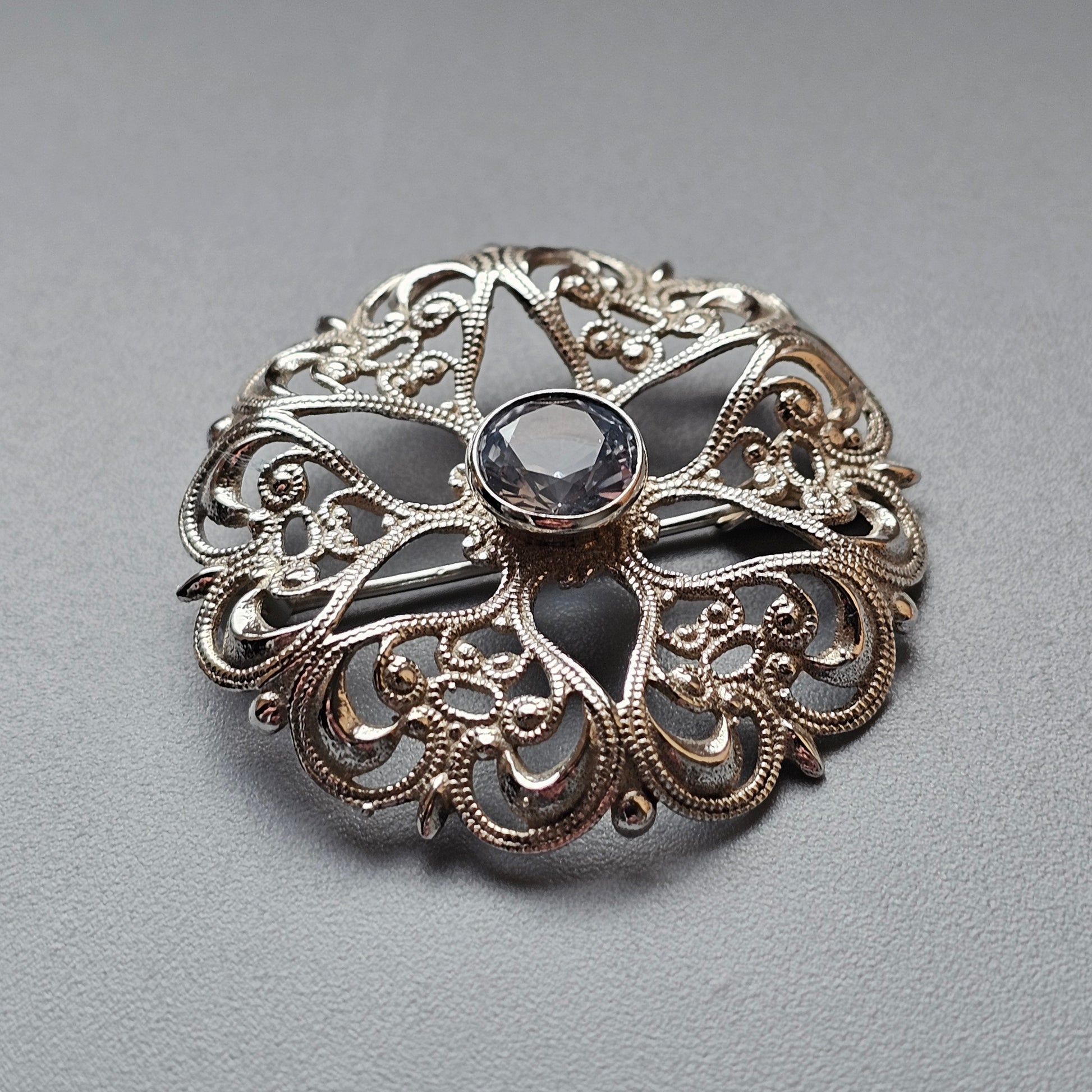 Ornate silver brooch with intricate filigree design and a central gemstone.