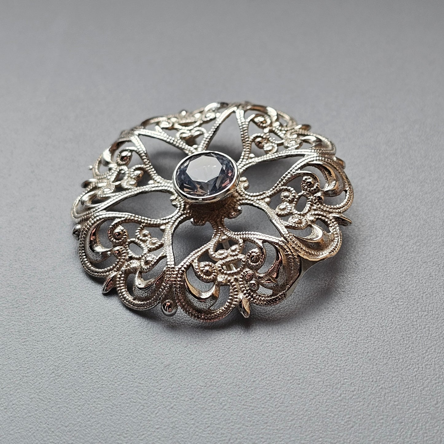 Ornate silver brooch with filigree design and central gemstone.