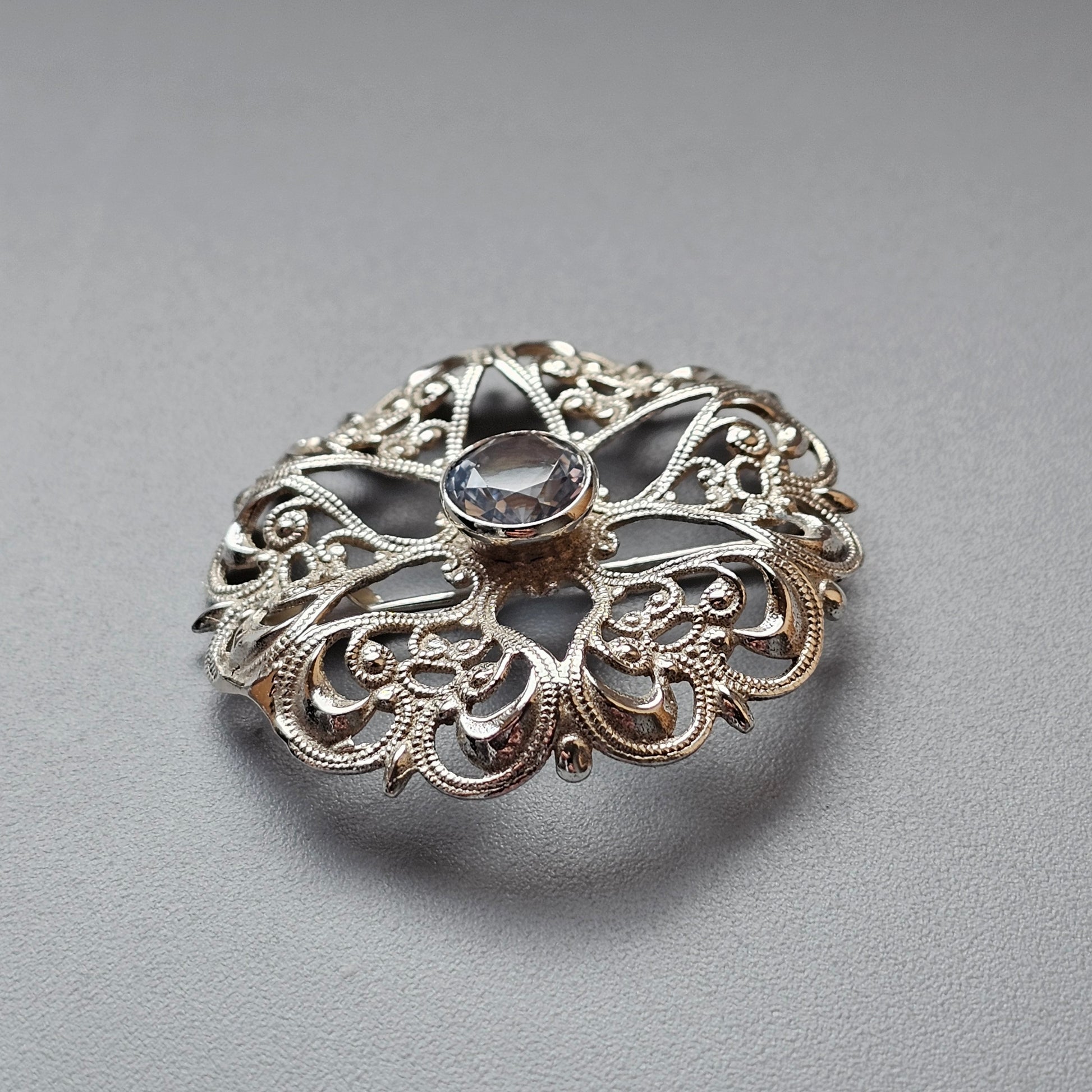 Ornate silver brooch with intricate filigree design and a central gemstone.