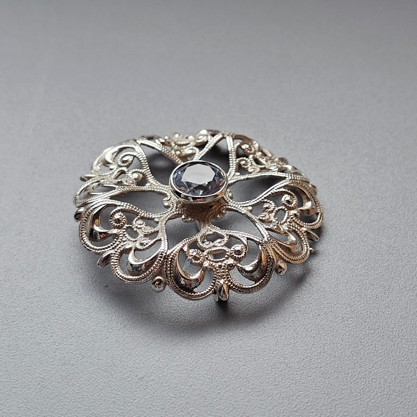 Ornate silver brooch with intricate filigree design and central gemstone.