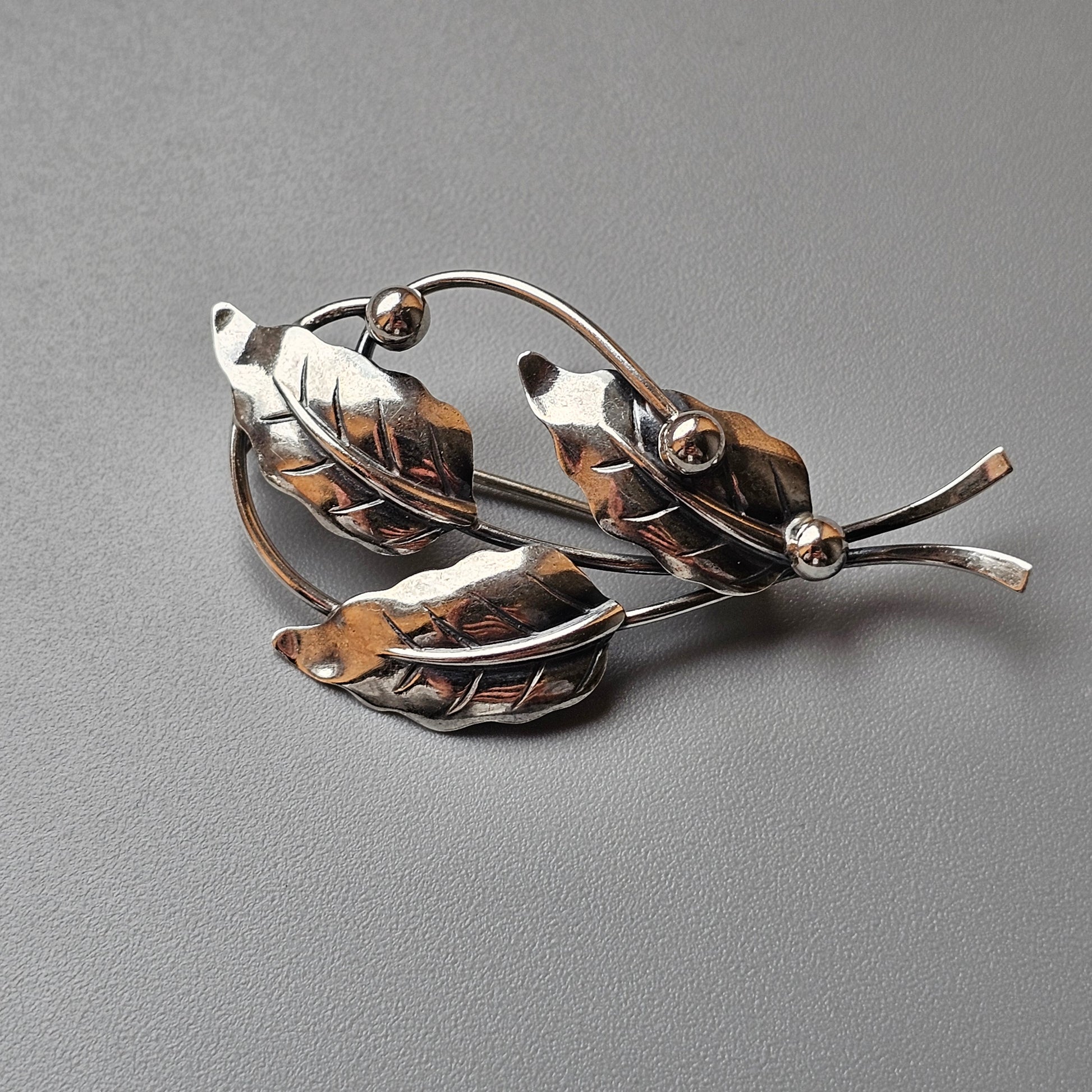 Vintage silver leaf-shaped brooch with three leaves and small decorative spheres.