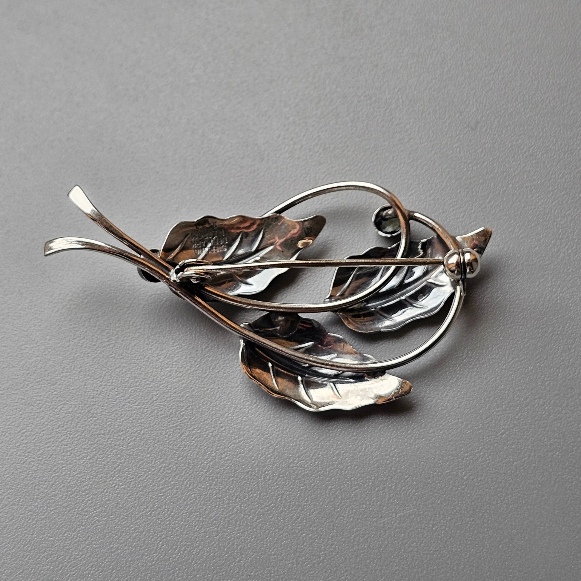 Intricately designed leaf-shaped brooch or pin made of mixed metals.