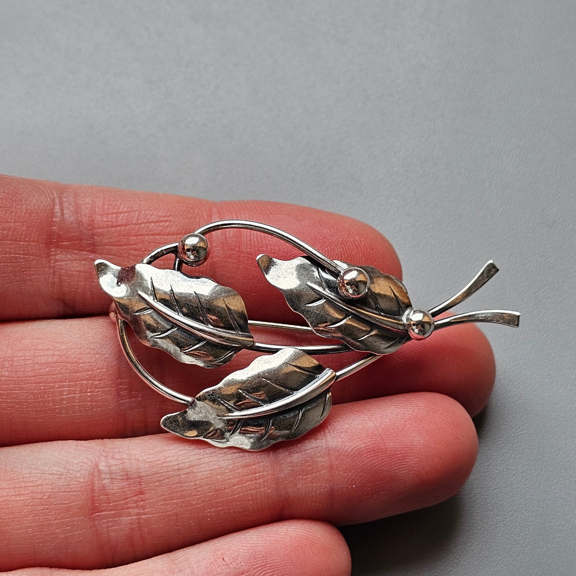 Silver leaf-shaped brooch with three leaves and small spherical accents.