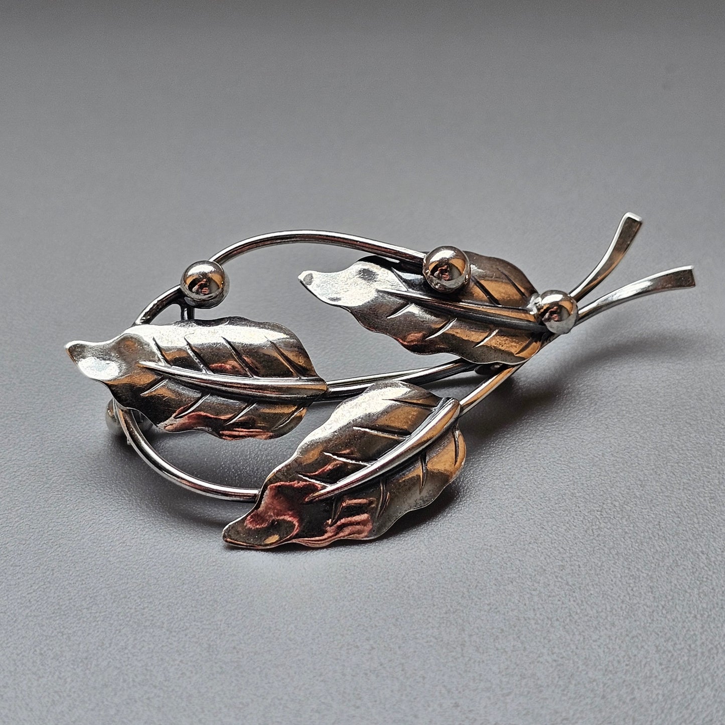 Metallic leaf-shaped brooch with multiple leaves and decorative spheres.