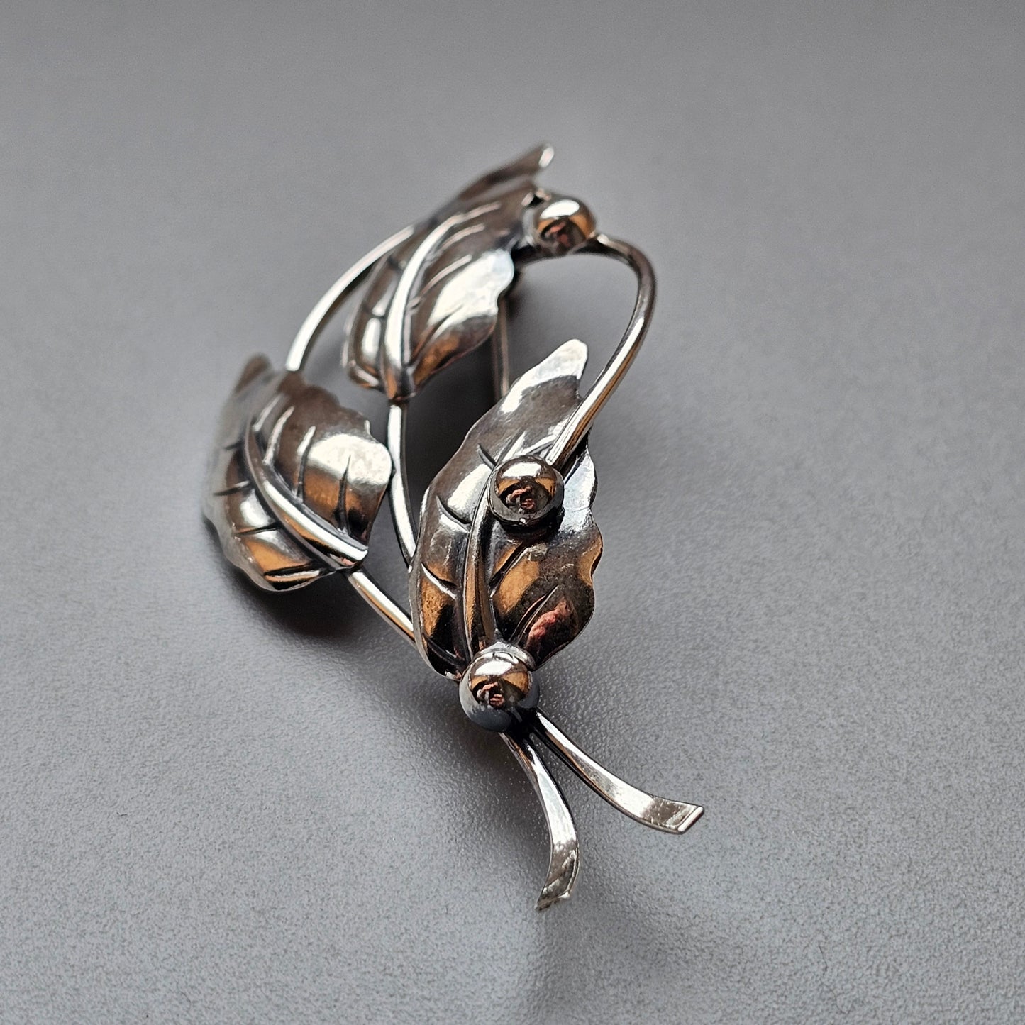 Silver-toned brooch or pin shaped like an abstract floral or leaf design with curved elements.