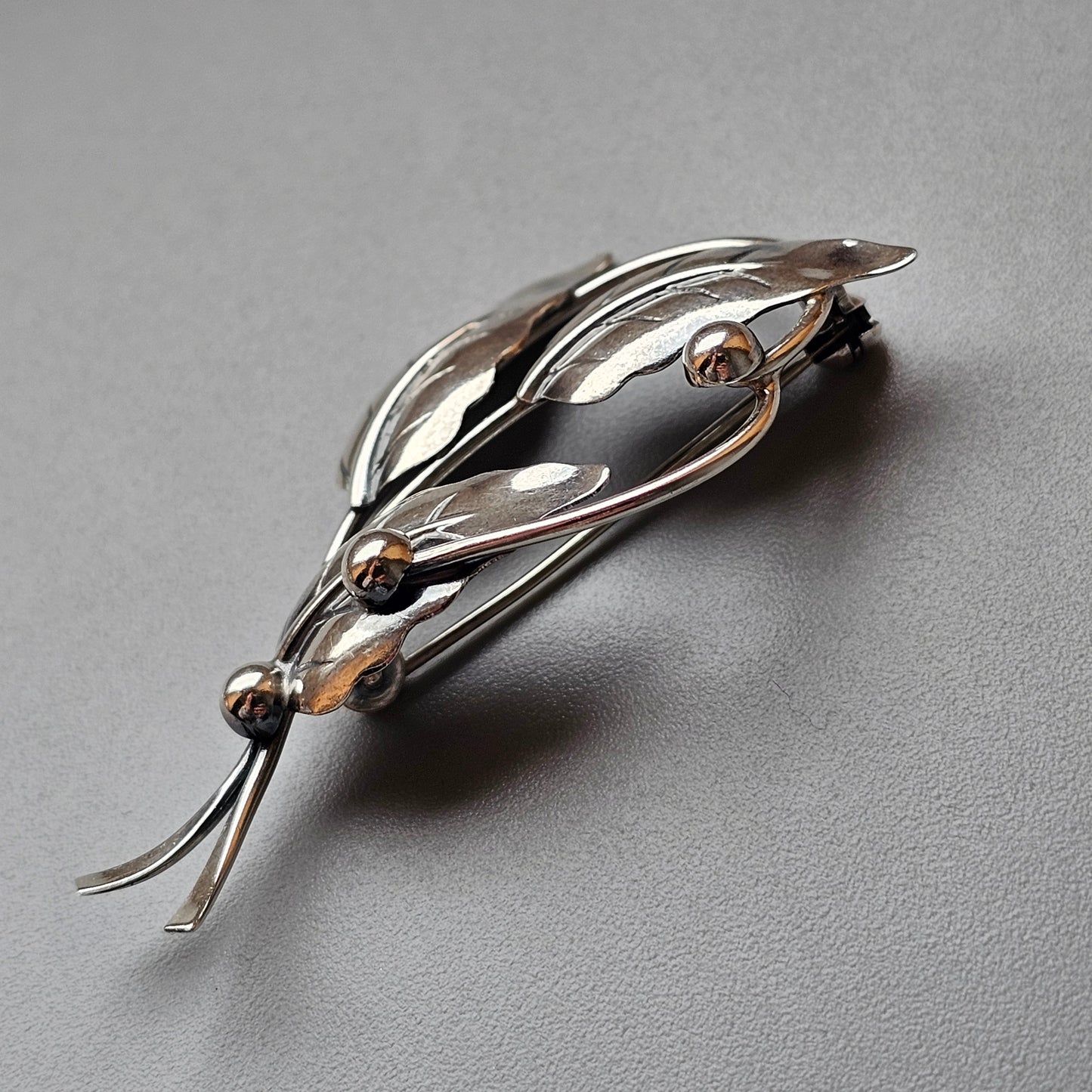 Silver leaf-shaped brooch with curved lines and small spherical accents.