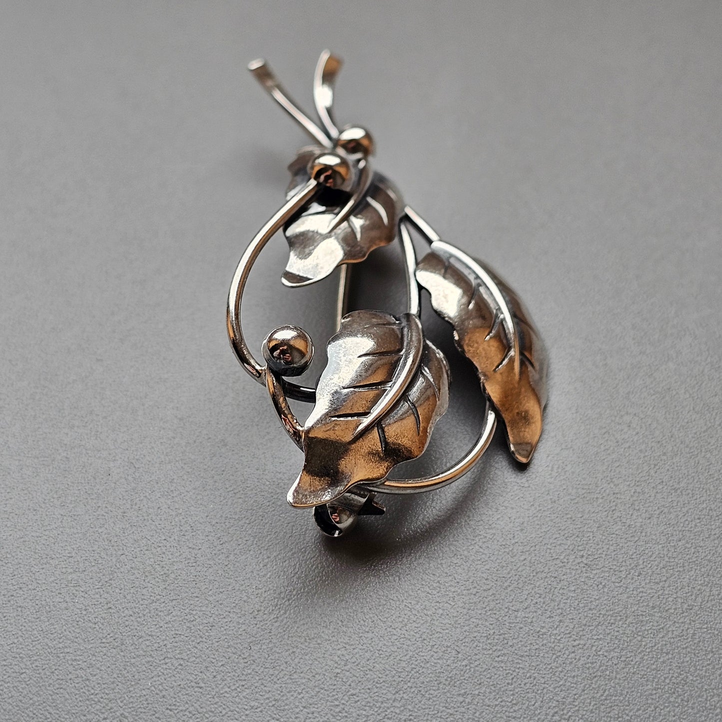 Silver brooch or pendant shaped like a stylized leaf or floral design with curving lines and organic forms.