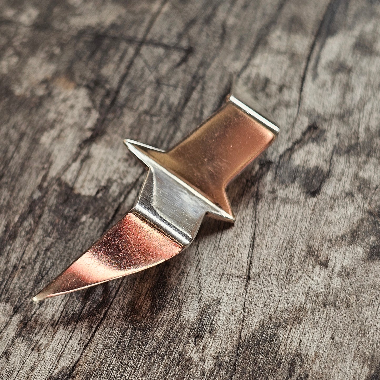 Metallic pin or brooch with a geometric, angular design in gold and silver tones.