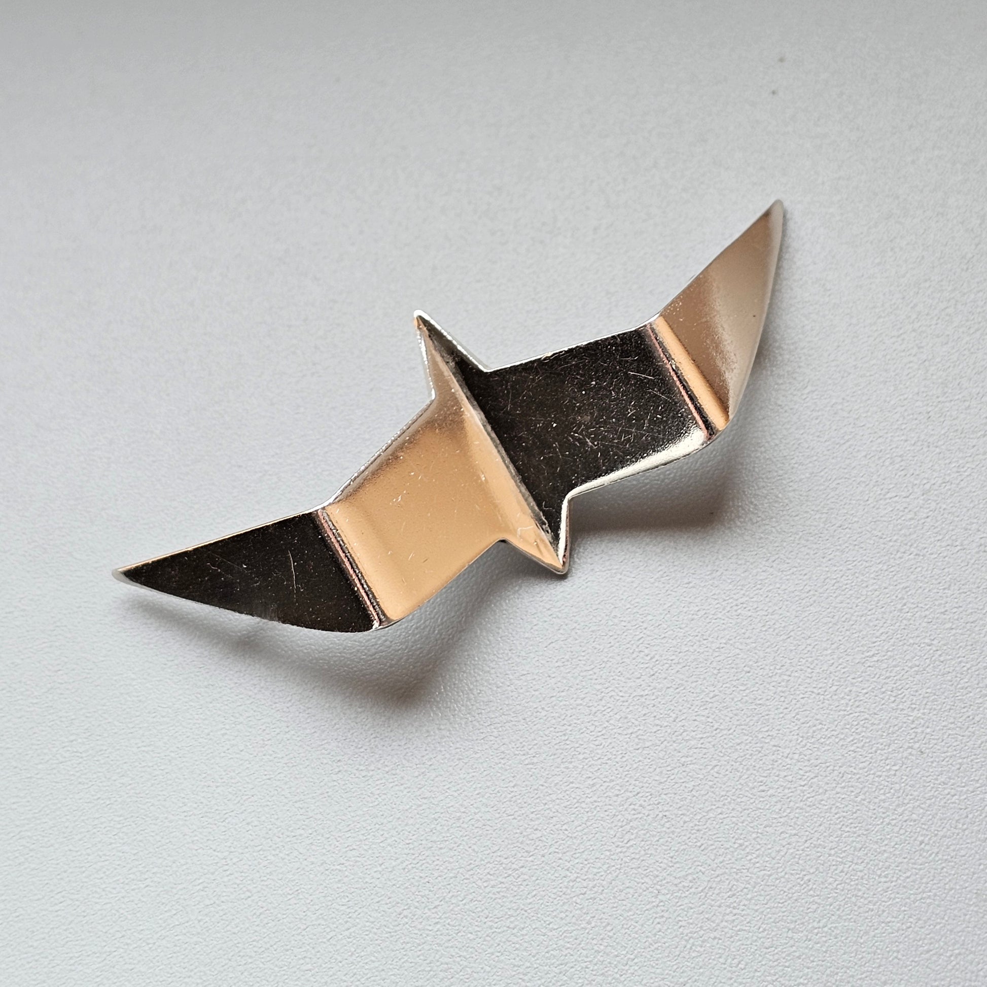 Metallic pin or brooch shaped like an abstract bird or wing design.