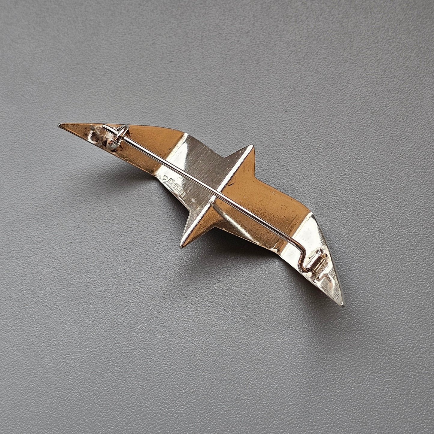 Metallic brooch or pin shaped like a stylized bird in flight.