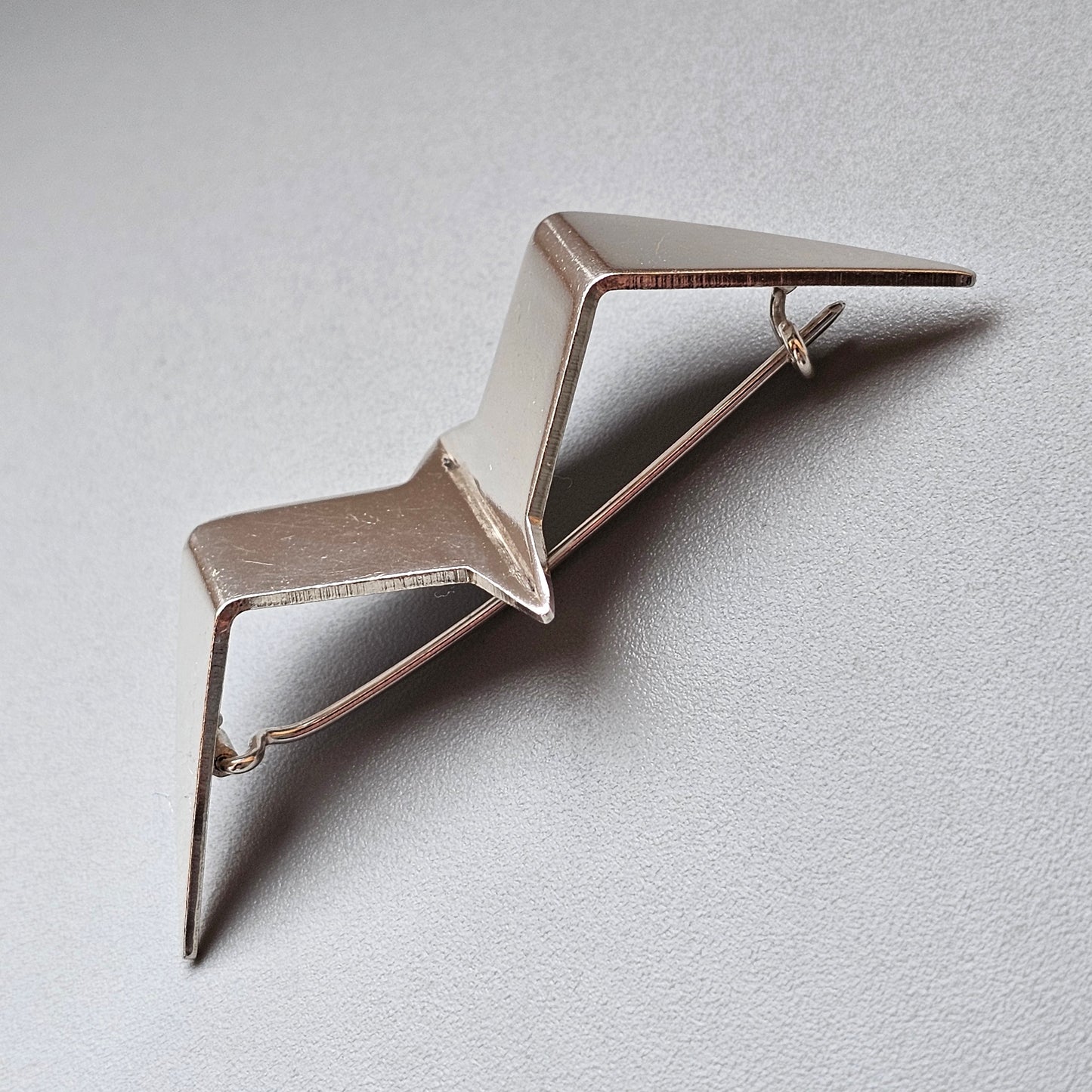 Metallic origami-style bird or airplane brooch with angular wings.