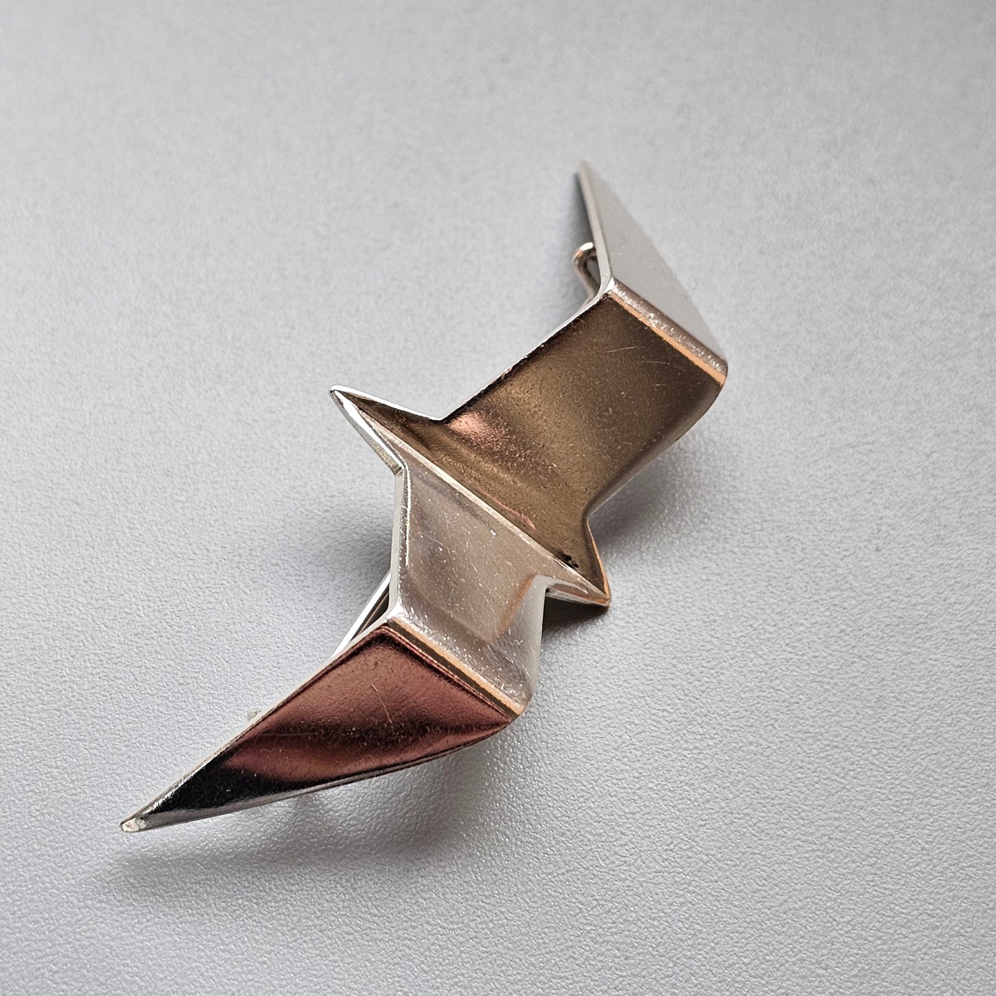 Metallic zigzag-shaped brooch or pin with a shiny, angular design.