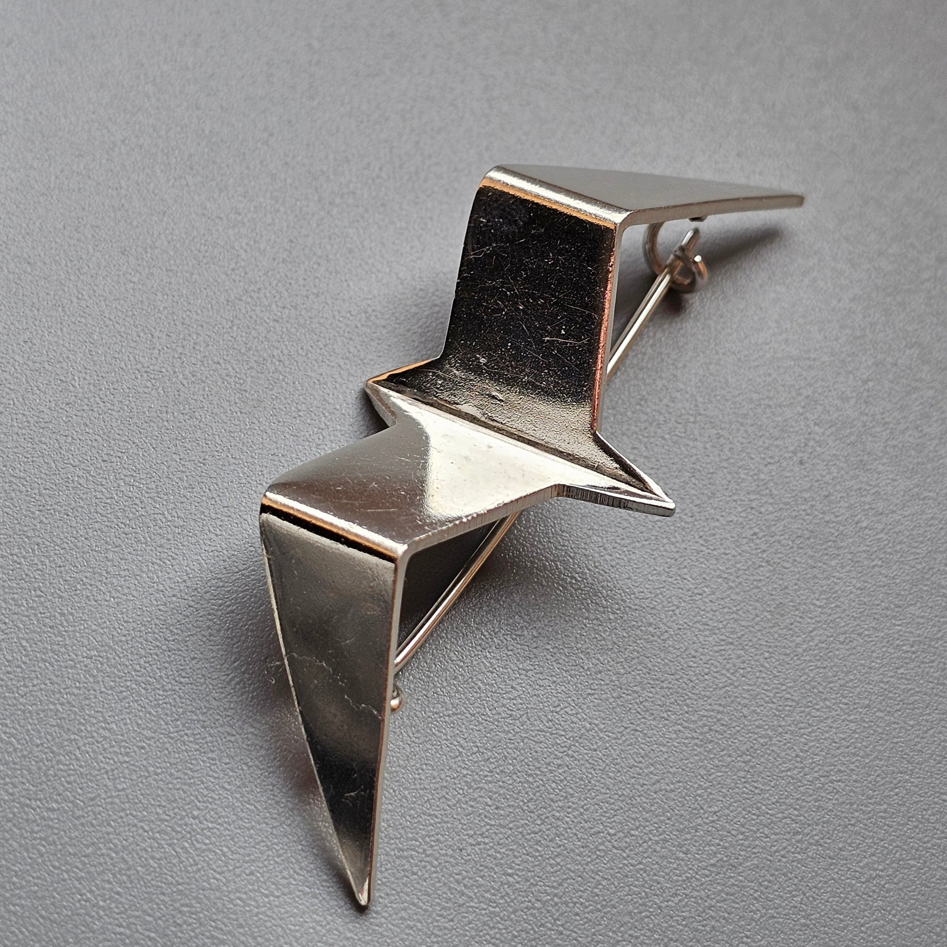 Silver metallic brooch shaped like an abstract bird in flight.