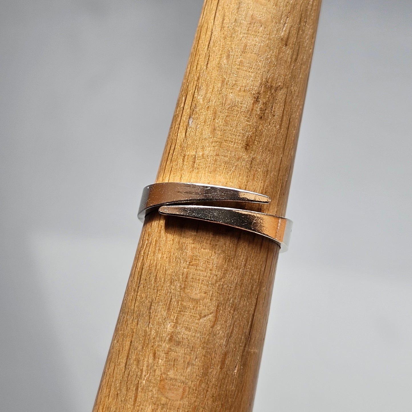 Silver ring with a split design wrapped around a wooden cylinder.