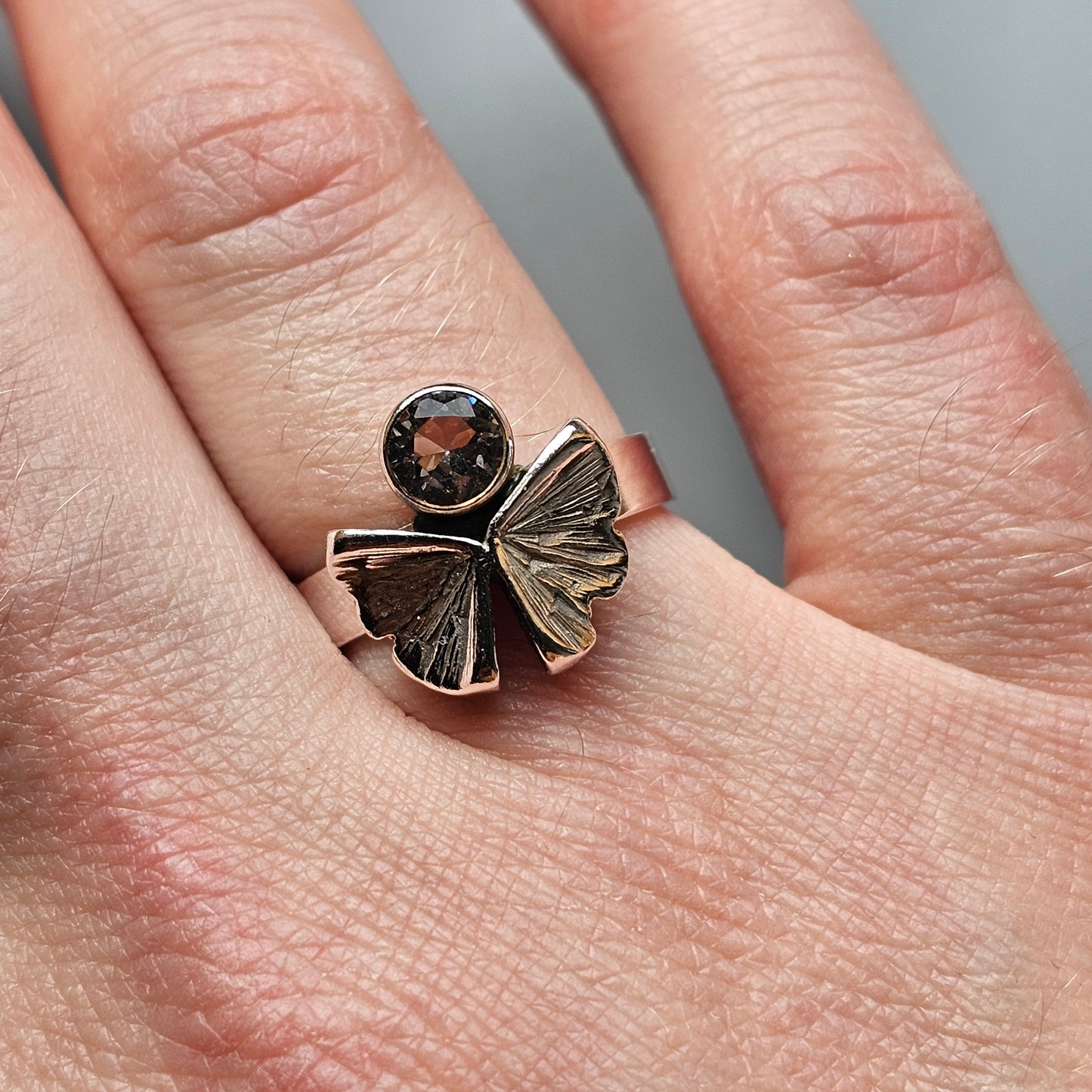 Butterfly-shaped ring with a gemstone at its center worn on a finger.