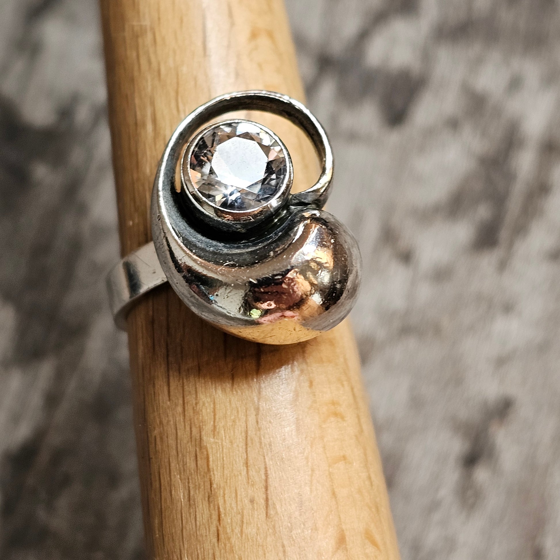 Silver ring with a spiral design and a single clear gemstone.