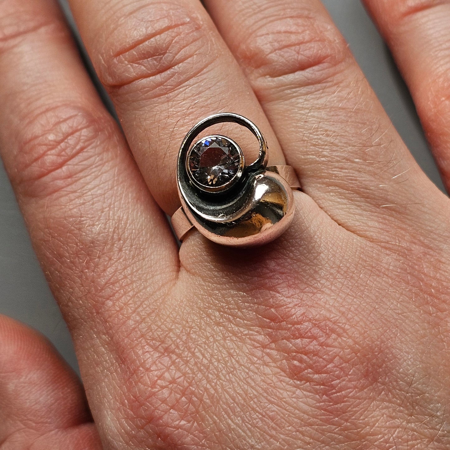 Unique silver ring featuring a swirling design with a dark stone or gem at its center.