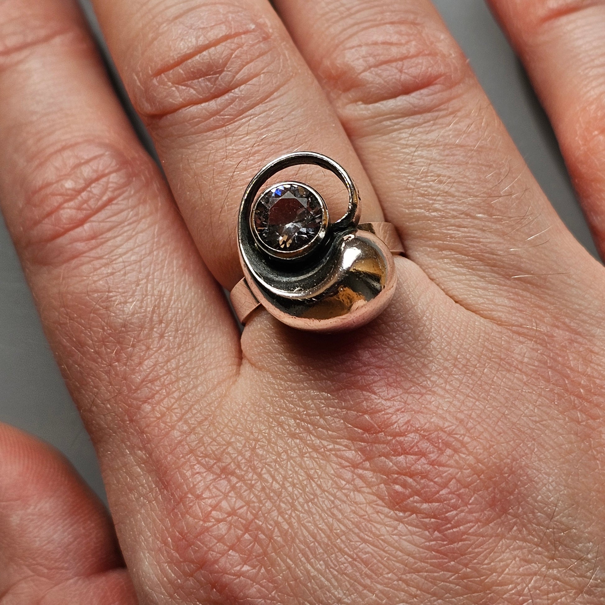 Unique silver ring featuring a swirling design with a dark stone or gem at its center.