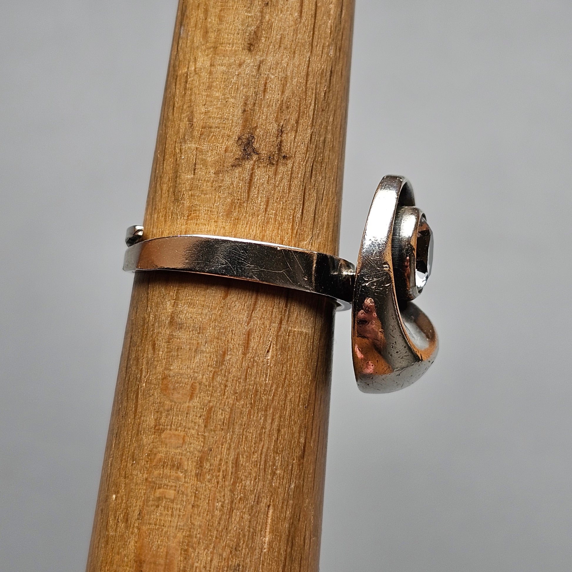 Silver ring with a curved design wrapped around a wooden pole or dowel.