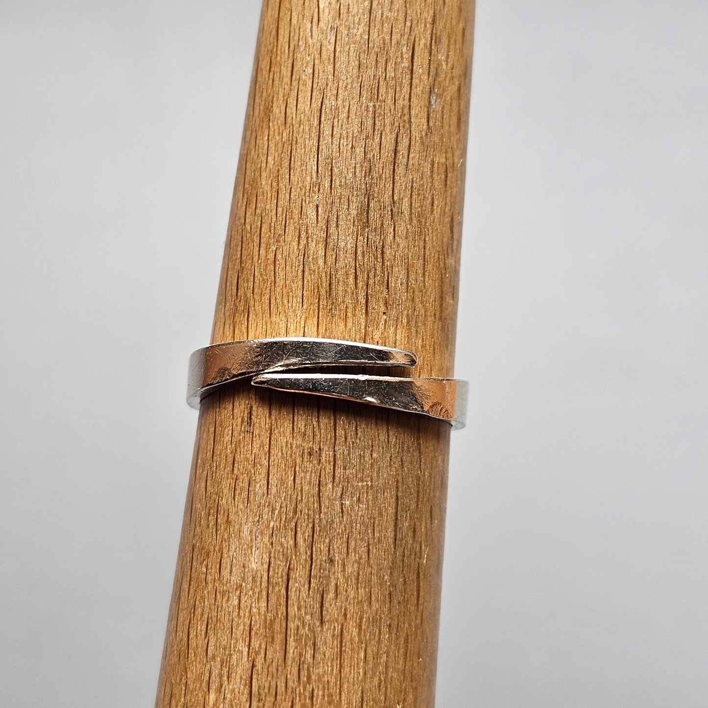 Silver ring with an overlapping, twisted design wrapped around a wooden cylinder.