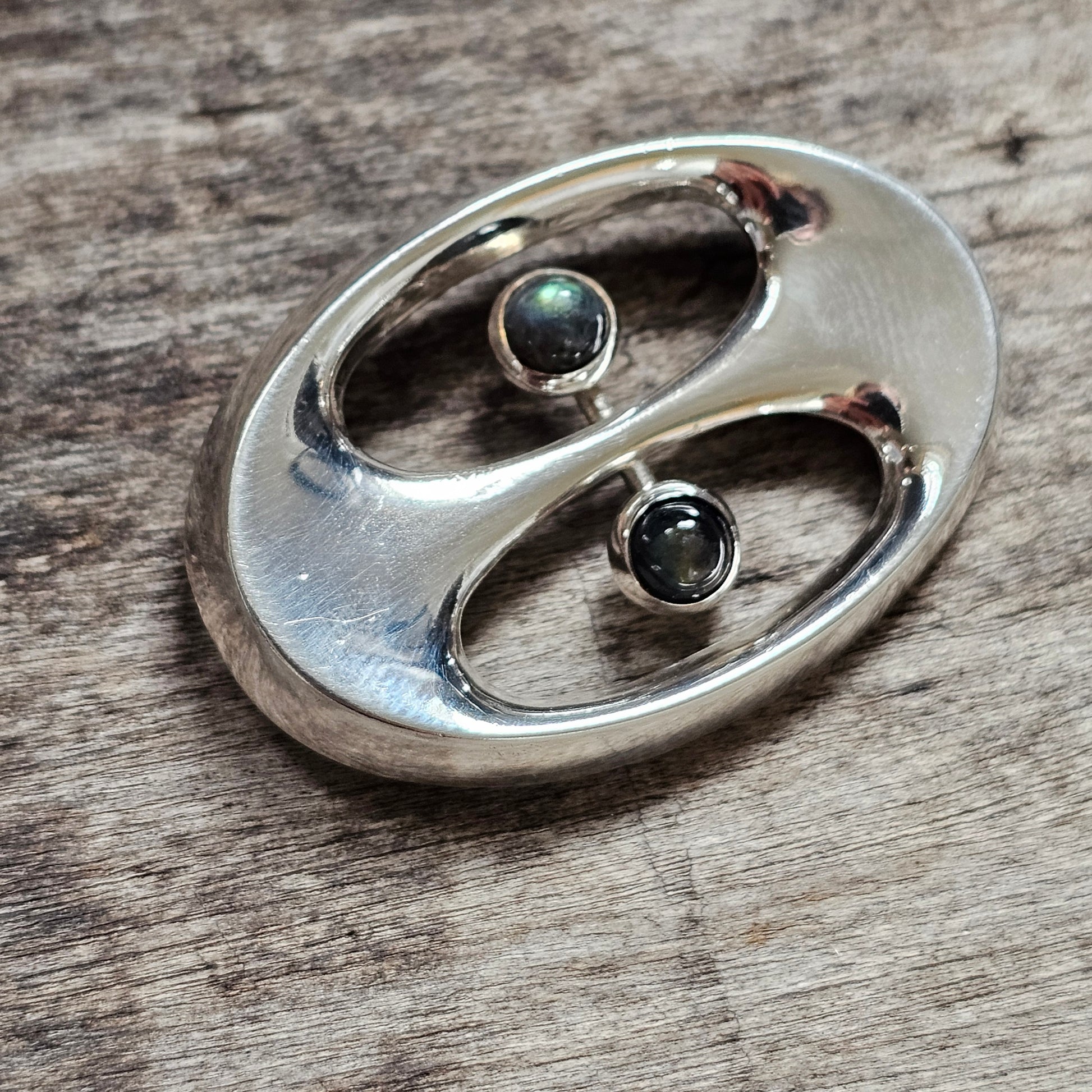 Silver pendant or brooch with an abstract yin-yang design featuring two small gemstones.