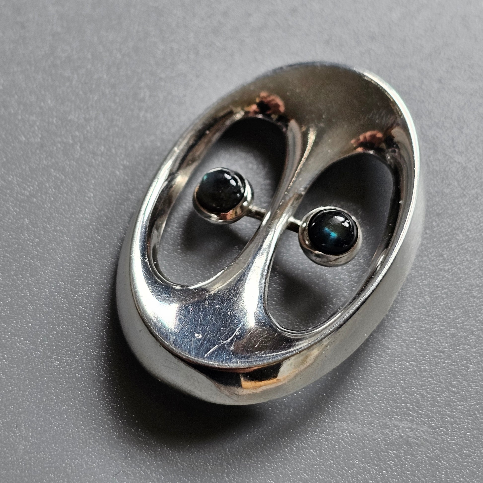 Metallic oval-shaped object with two eye-like openings containing dark spheres.