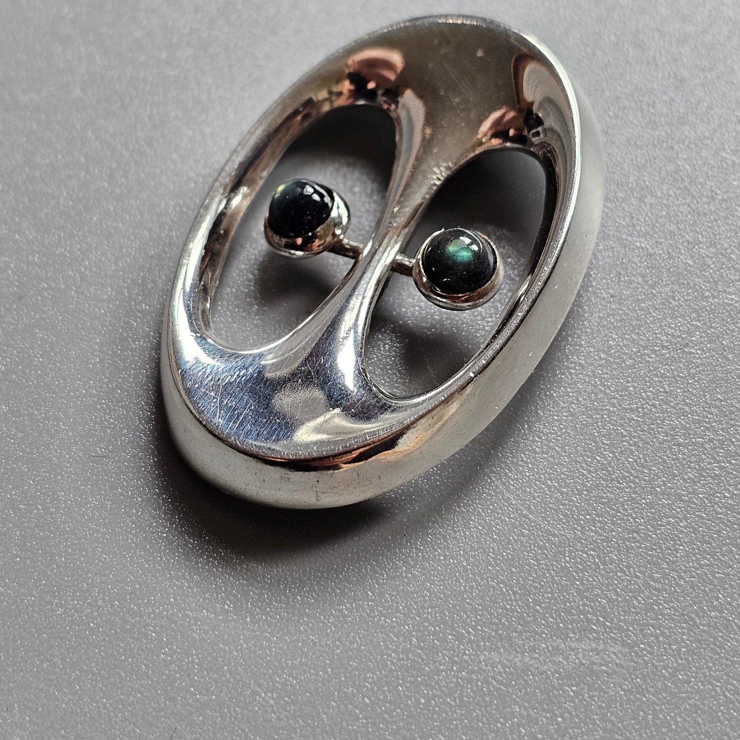 Oval-shaped metallic object with two eye-like indentations containing small spheres.