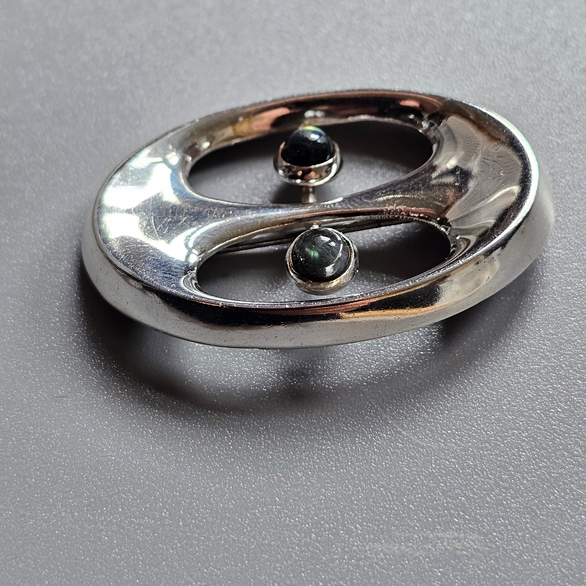 Shiny metallic oval-shaped object with two small dark spheres embedded in its surface.