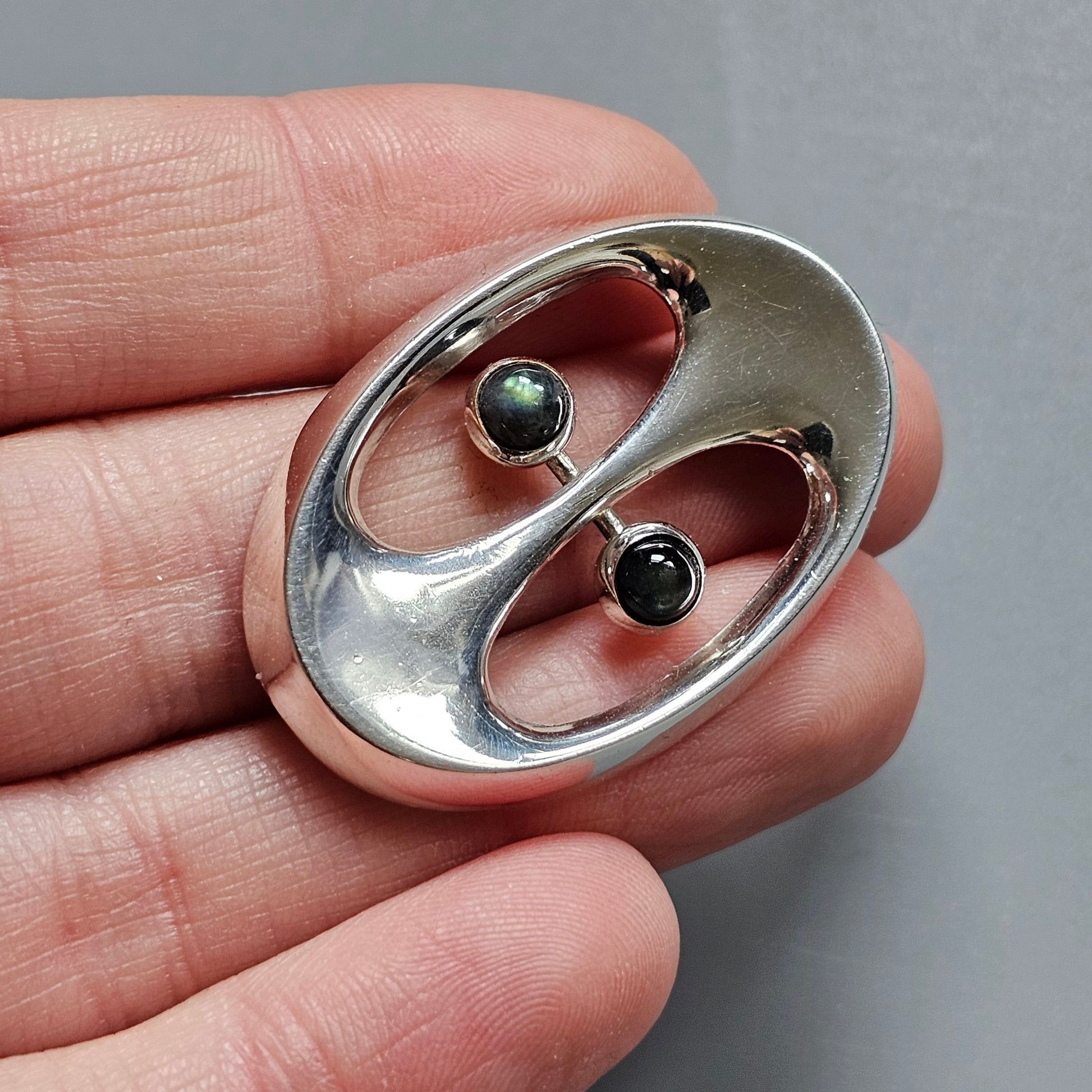 Silver oval-shaped pendant or brooch with two dark gemstones set in a yin-yang inspired design.