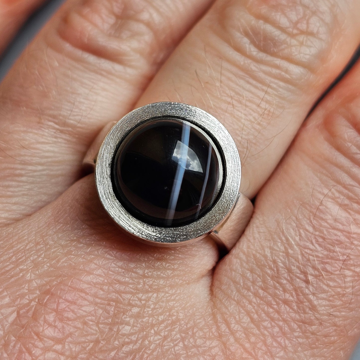 Silver ring with a round black stone or gem featuring a white cross-like pattern.