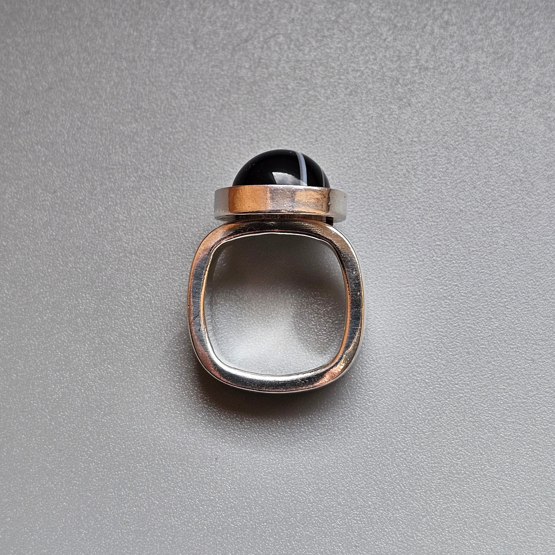 Modernist ring with a square silver band and round black stone.