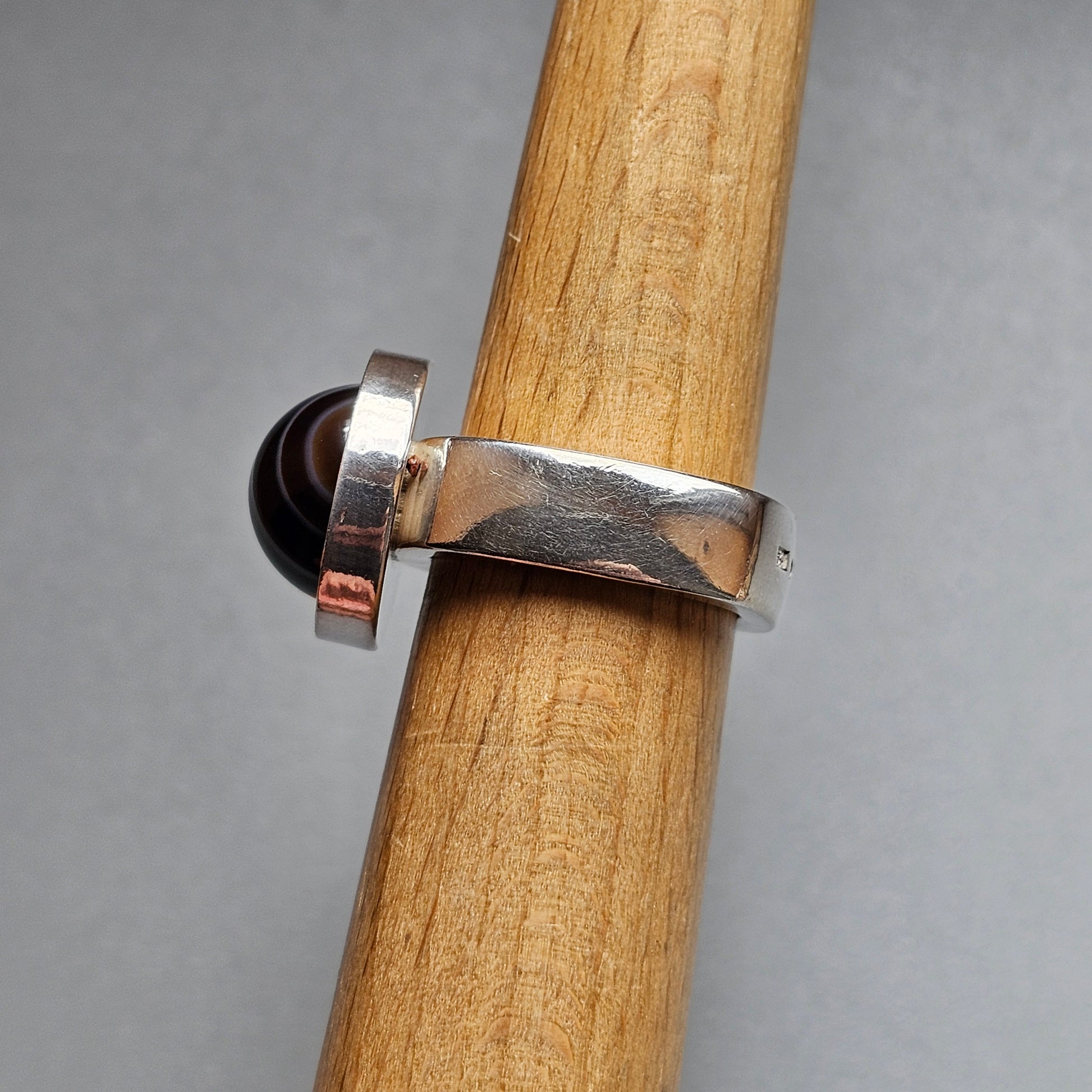 Silver ring with a black stone or bead, wrapped around a wooden dowel or rod.