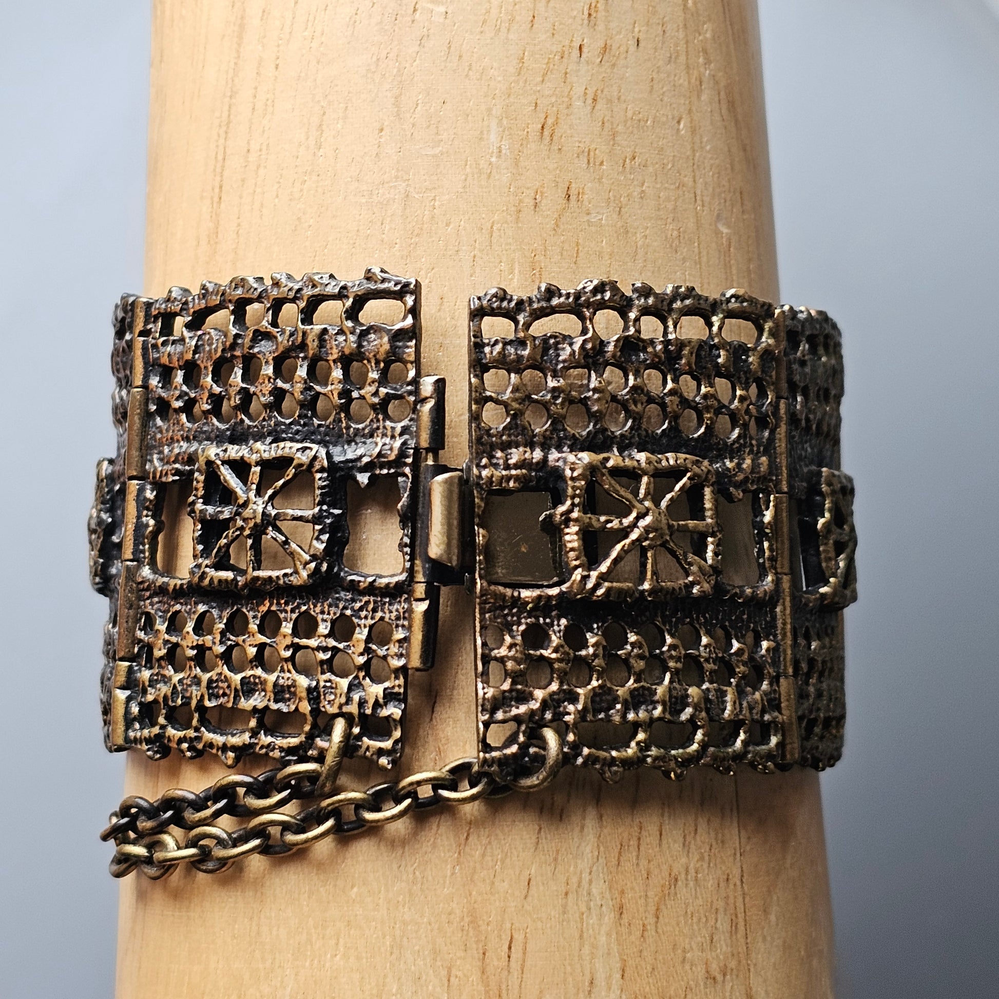 Ornate metal bracelet with intricate geometric patterns and a chain attachment.