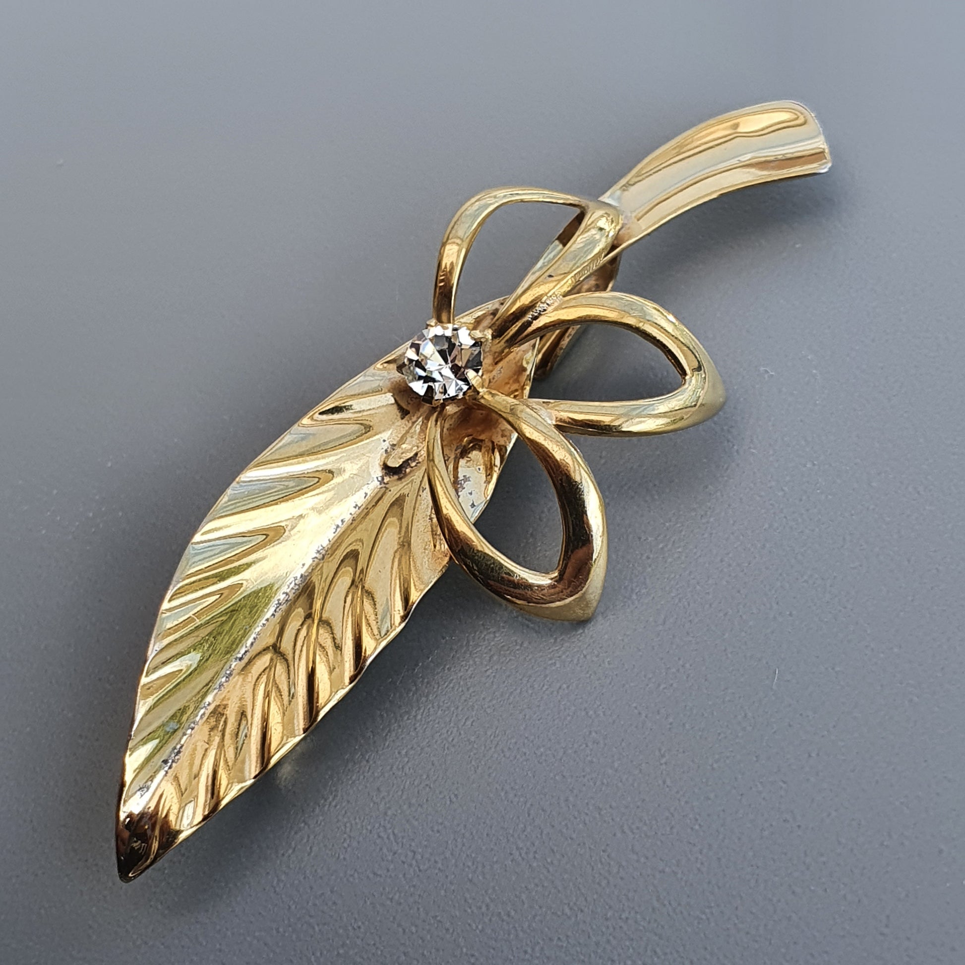 Gold leaf-shaped brooch with a small diamond accent.