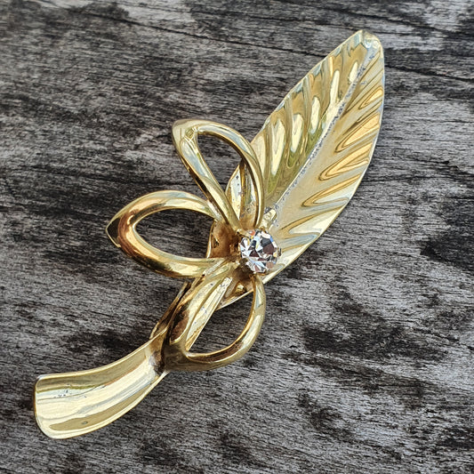 Gold-toned leaf-shaped brooch with a small gemstone accent.