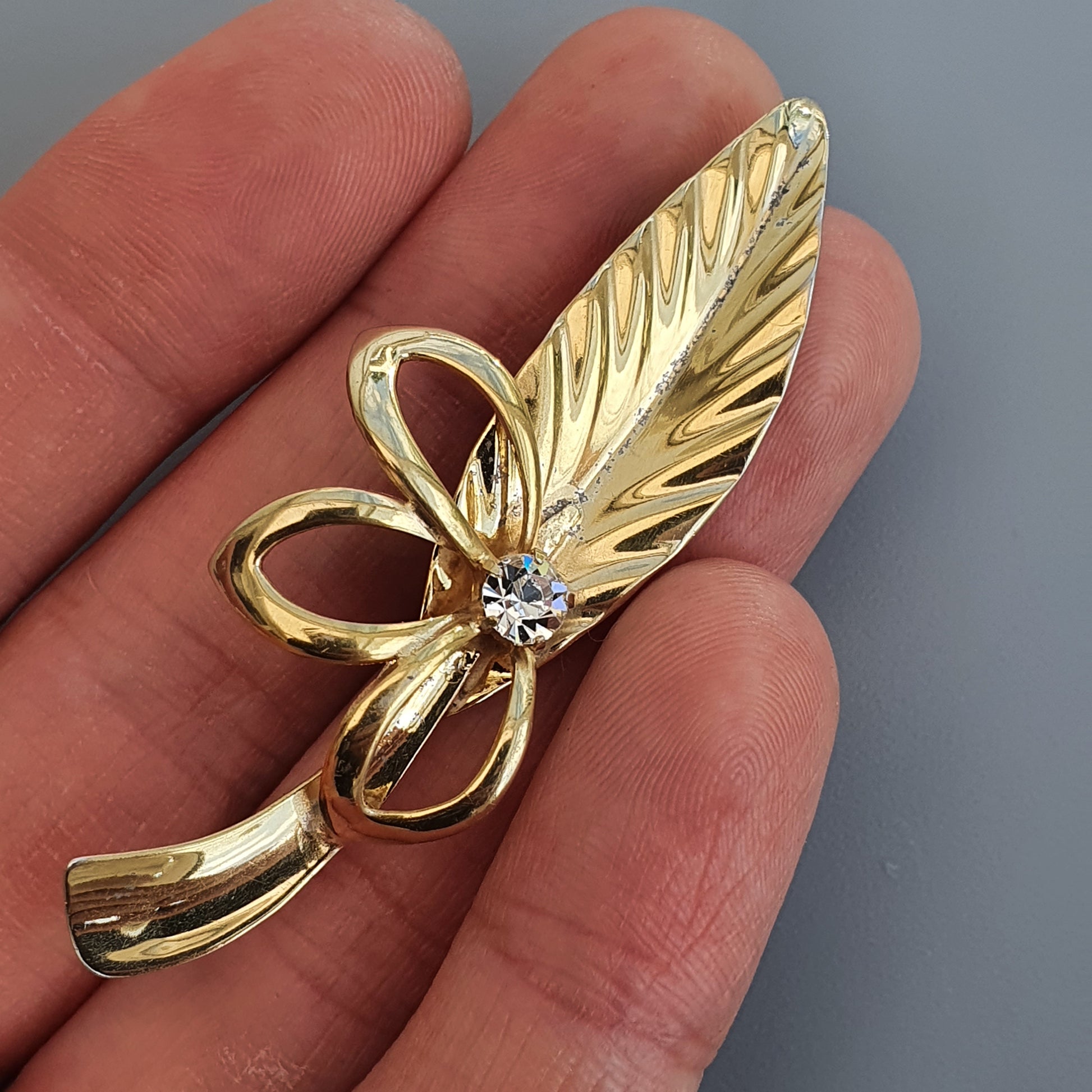 Gold-toned brooch shaped like a feather with a small gemstone accent.