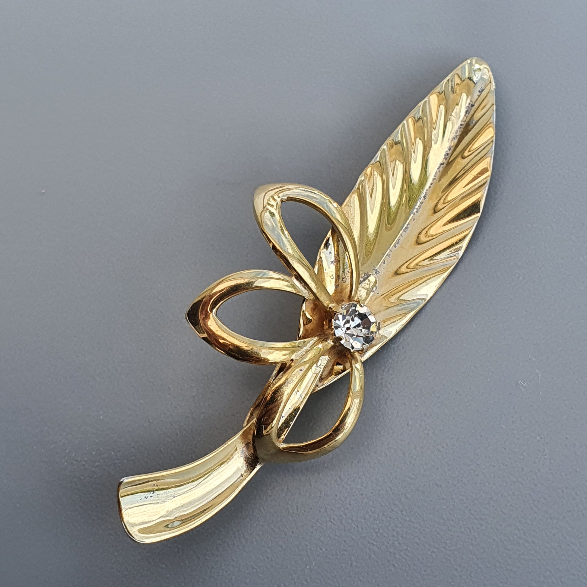 Gold-toned leaf-shaped brooch with a small diamond accent.