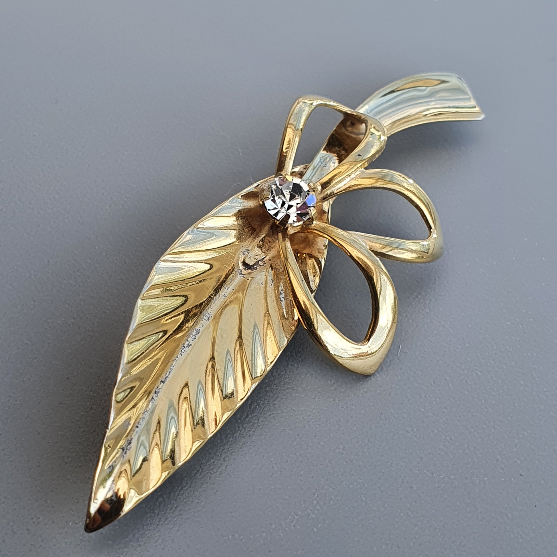 Gold-toned leaf-shaped brooch with a small gemstone accent.