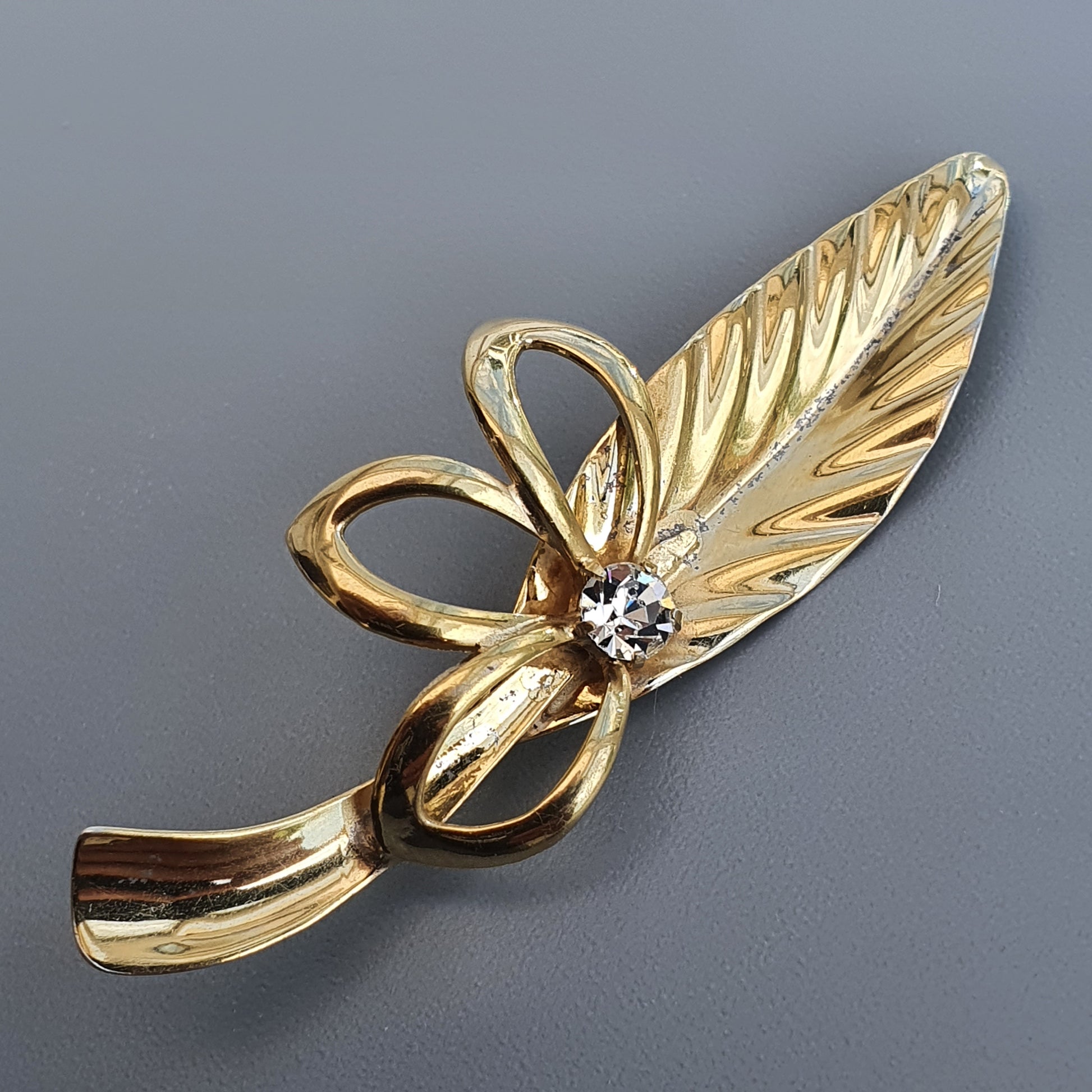 Gold-toned leaf-shaped brooch with a small diamond accent.