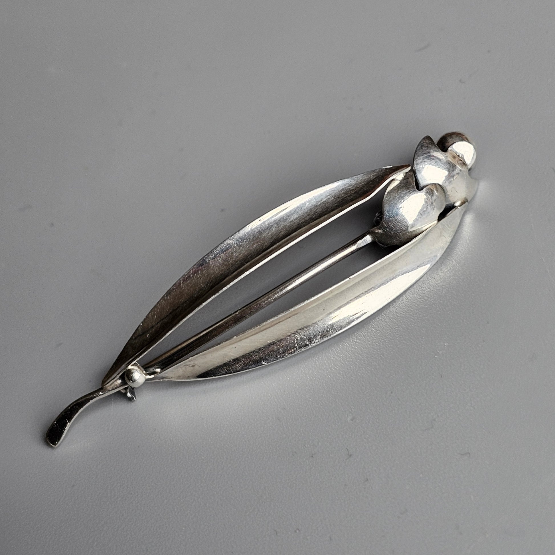 Silver brooch or pin shaped like an abstract leaf or petal with spherical accents.