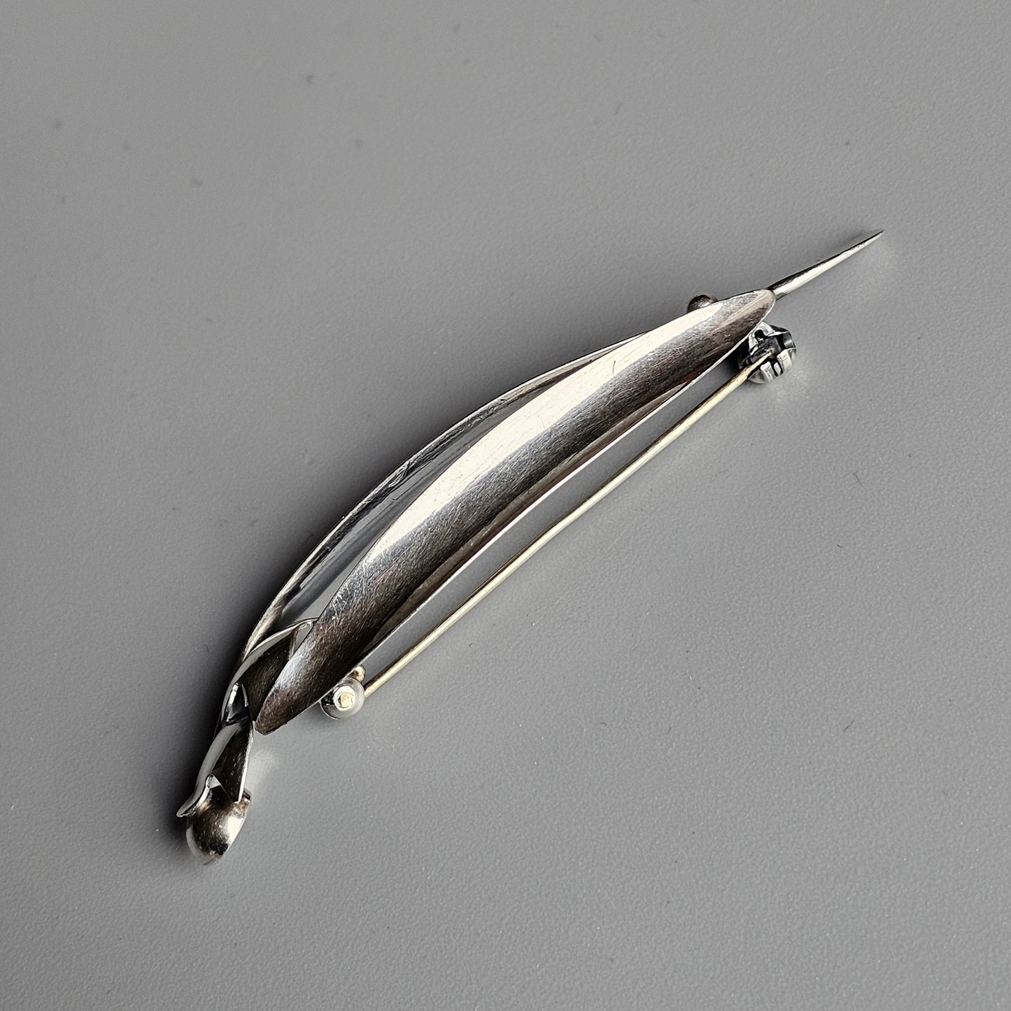 Silver brooch shaped like a stylized leaf or feather with a pin clasp.