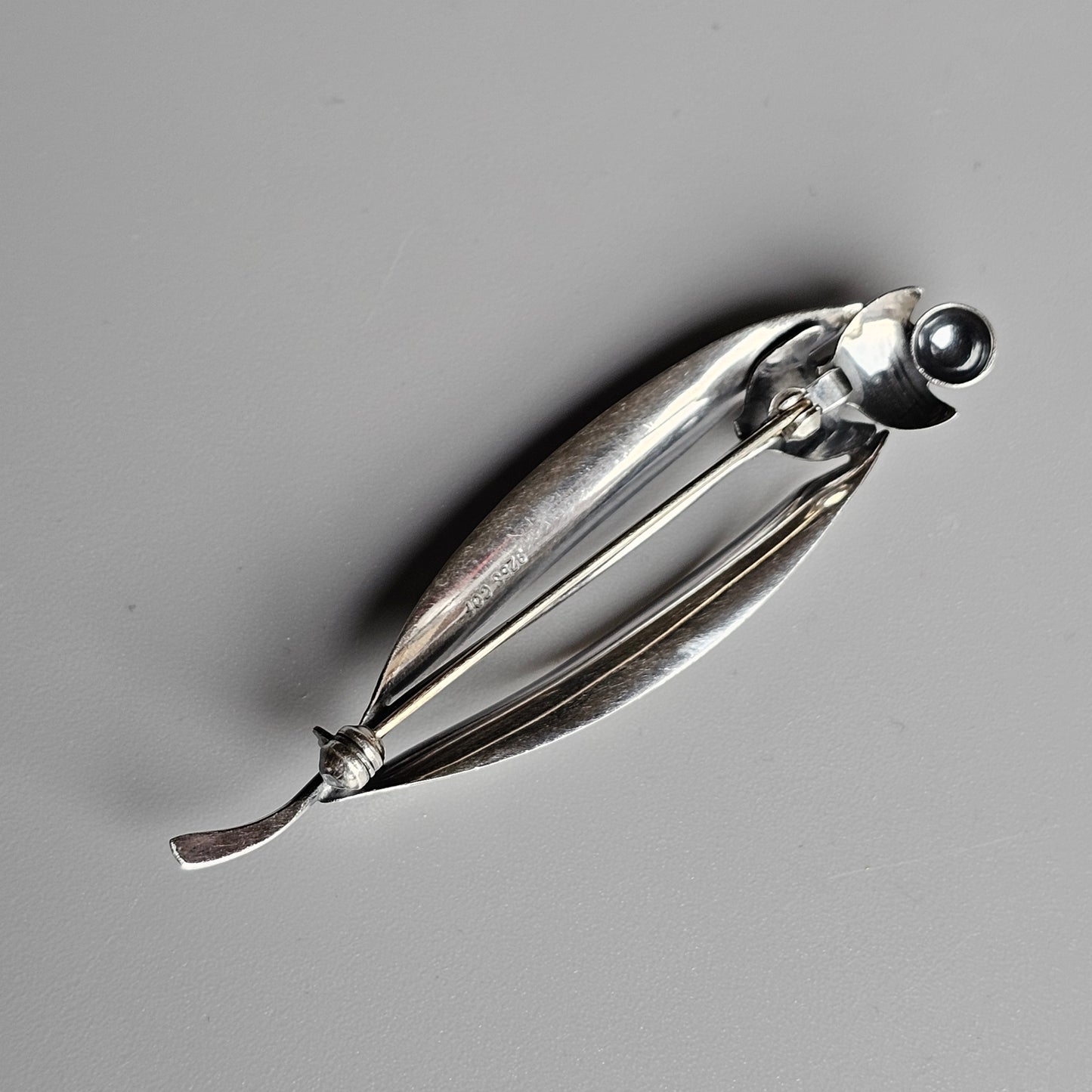 Sleek, elongated silver fish-shaped brooch or pin with a spherical eye detail.