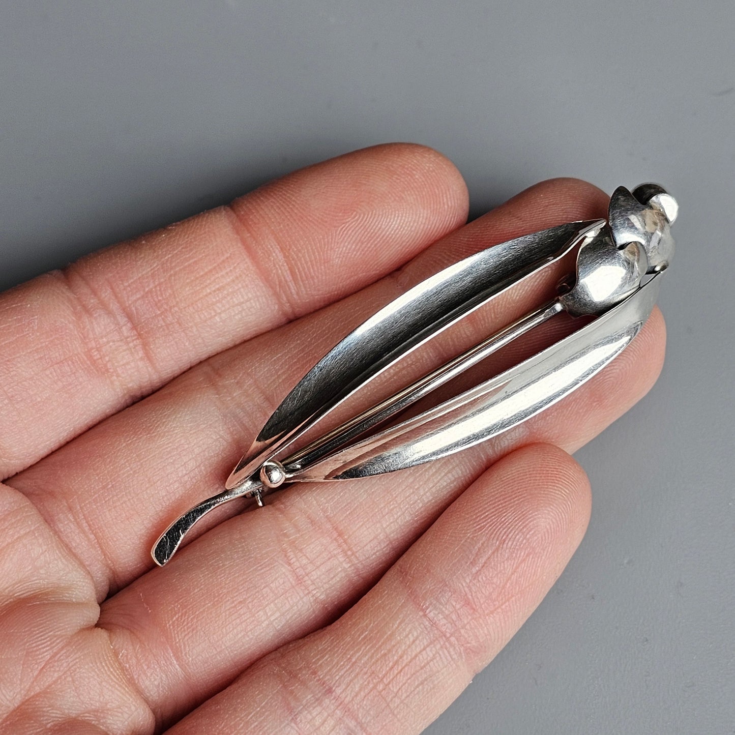 Silver brooch shaped like an elongated leaf or pod with a pearl accent.