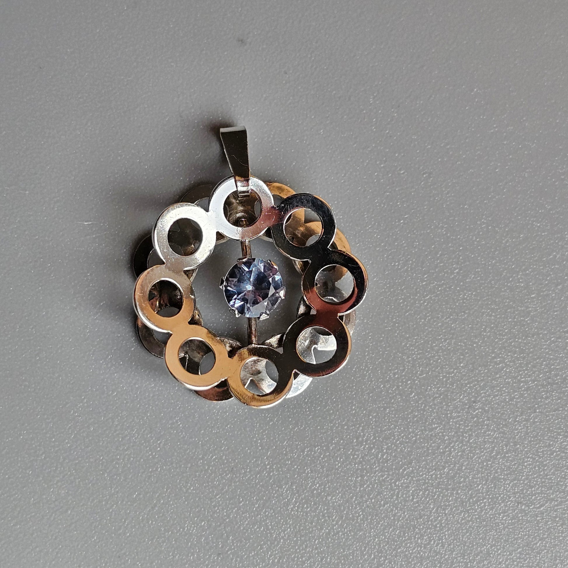 Circular pendant with metallic rings and a central gemstone.