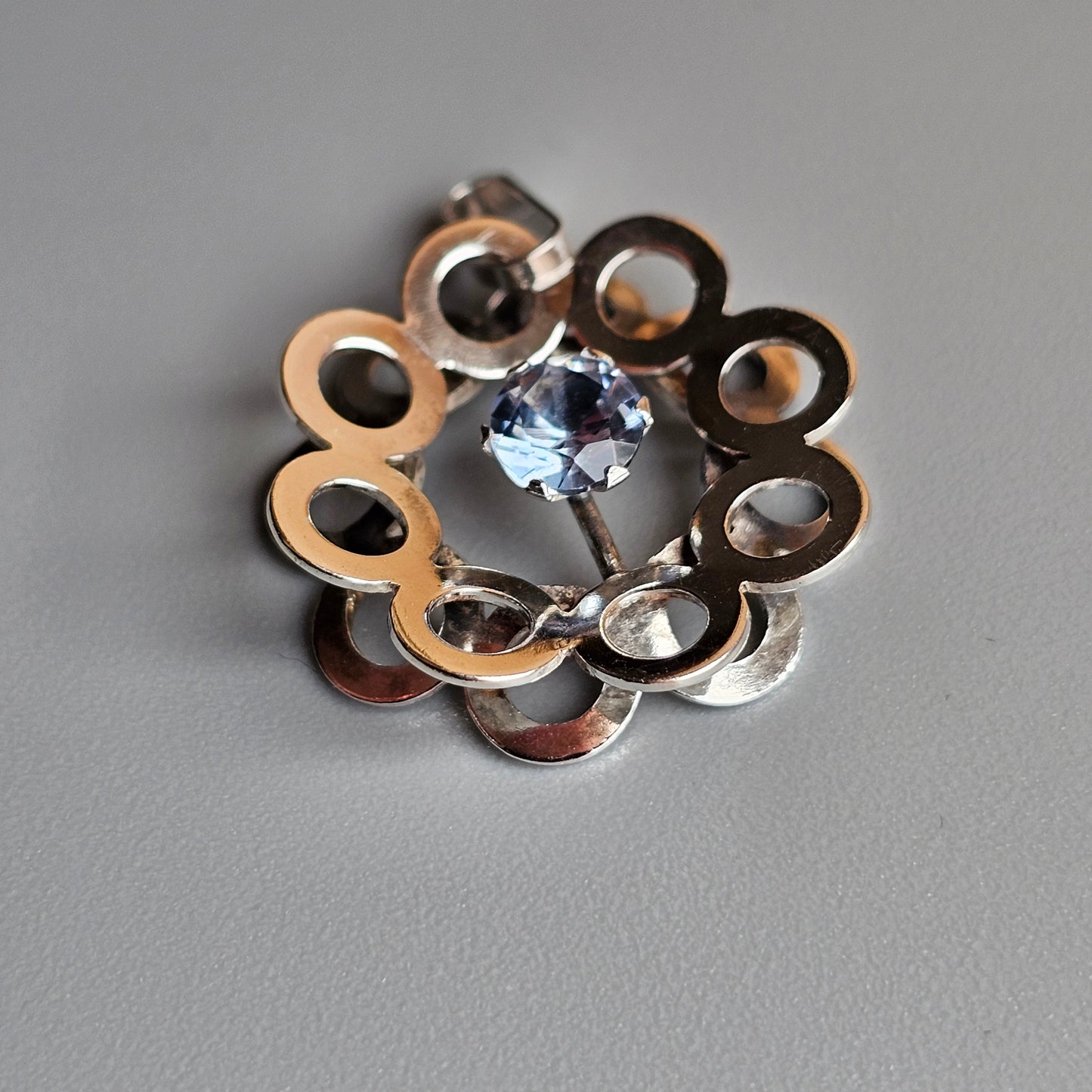 Metallic flower-shaped brooch or pendant with a light blue gemstone at its center.